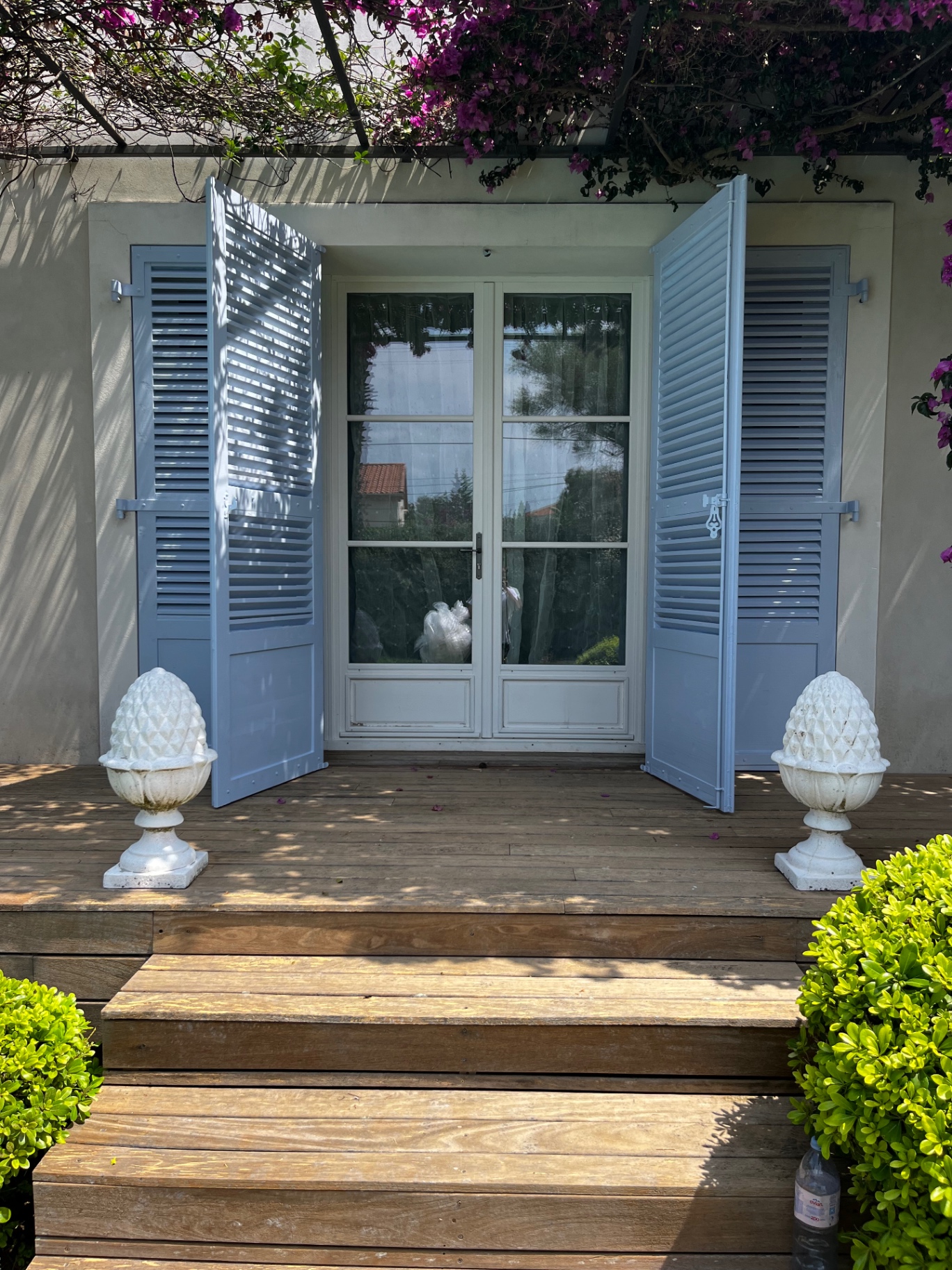 LUX RENOV — porte-fenêtre encadrée par les volets bleus finis, escalier en bois et pots décoratifs