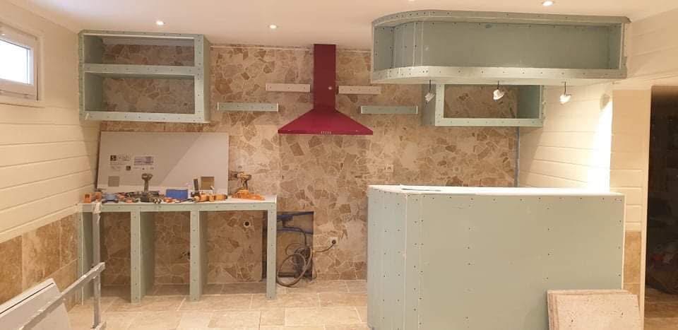LUX RENOV — cuisine d'été pool house avec mur en pierre travertin, hotte rouge et meubles placo
