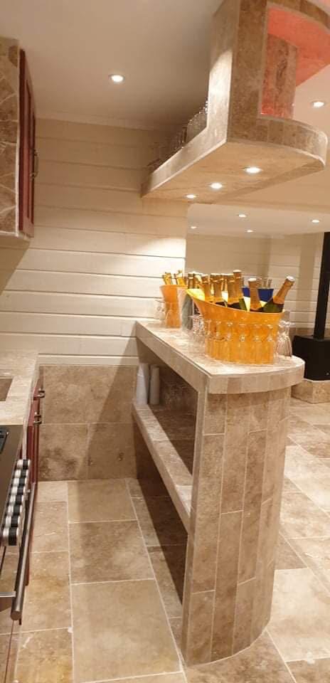 LUX RENOV — bar arrondi en pierre travertin avec seaux à champagne et spots LED